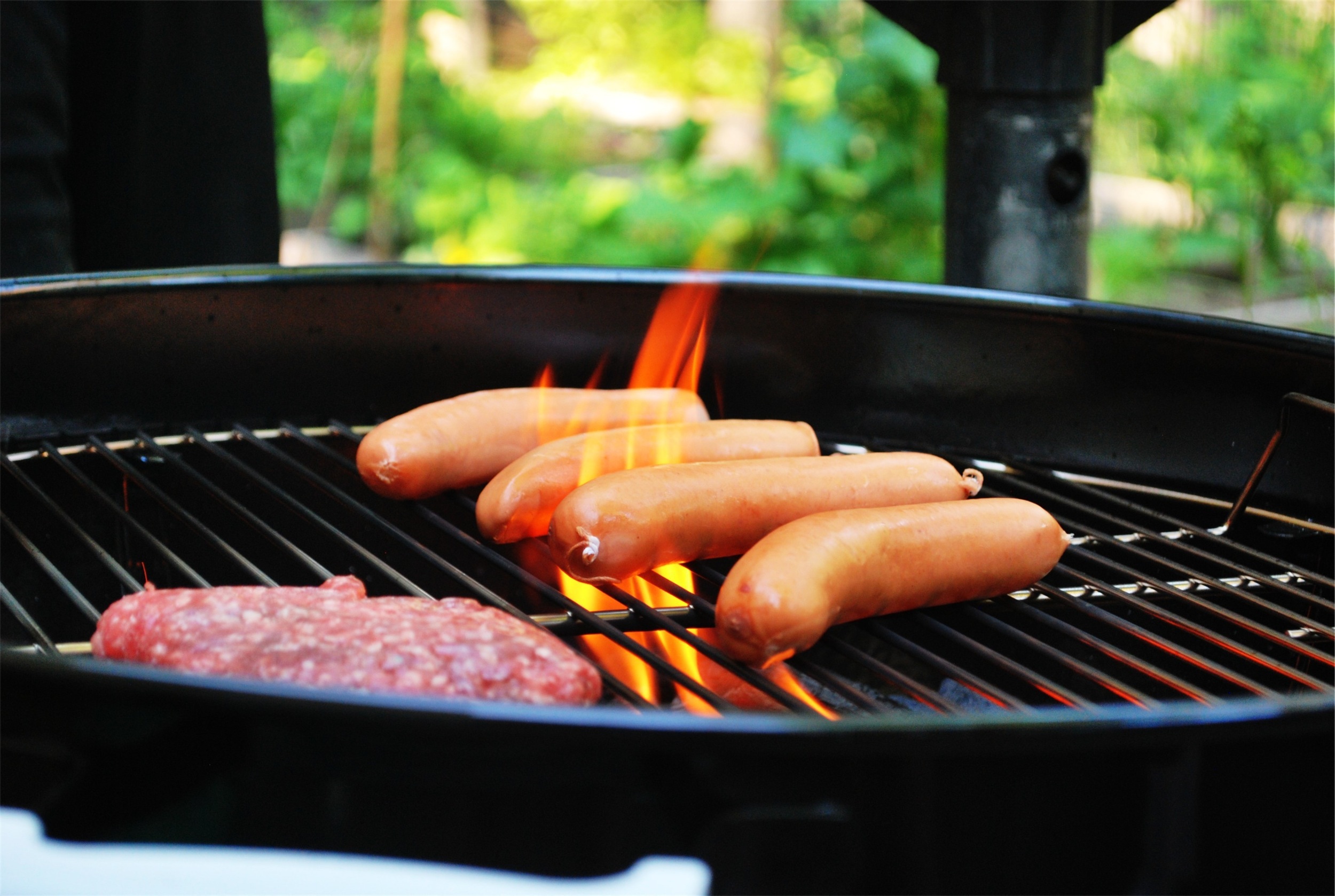 Image of charcoal barbecue grill with four hotdogs and a hamburger with flame licking up between grate.